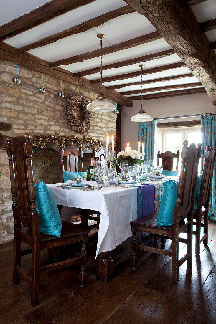 Türkisfarbene Kissen auf Esszimmerstühlen unter einer Balkendecke in einem Haus in den Cotswolds, UK