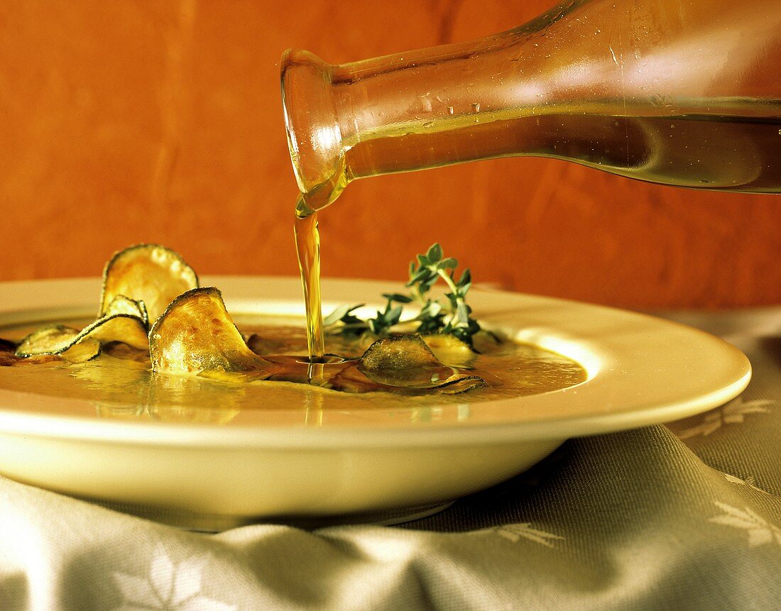Olivenöl wird in Zucchinisuppe gegossen