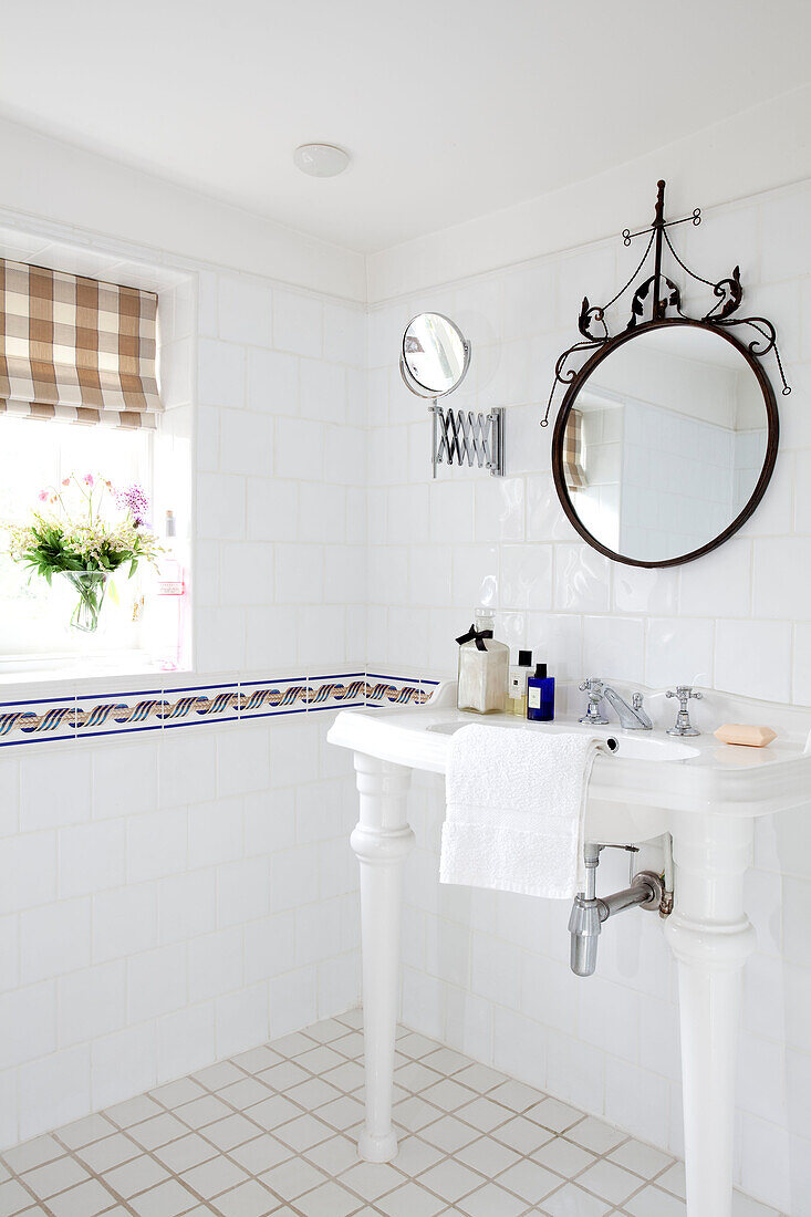 Circular mirror above washbasin in white tiled bathroom in East Sussex home, England, UK