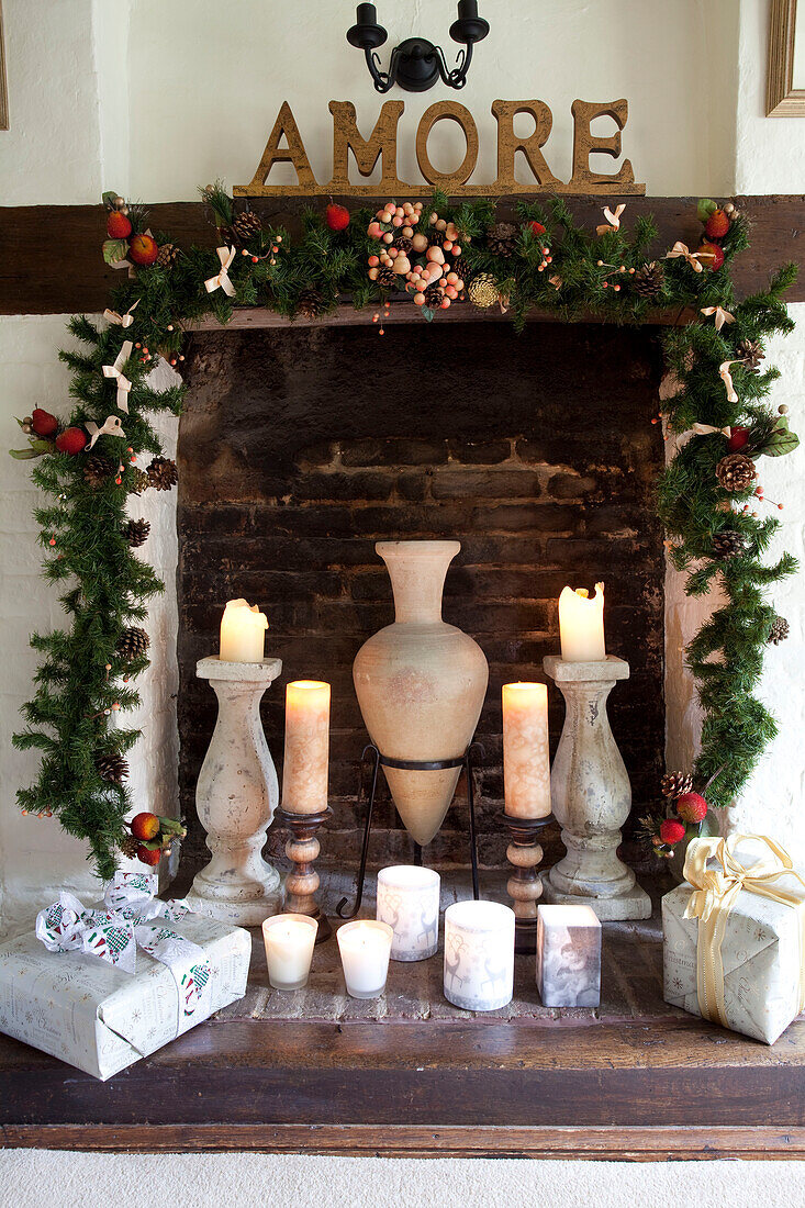 Beleuchtete Kerze und Geschenke im gemauerten Kamin mit Weihnachtsgirlande Sussex UK