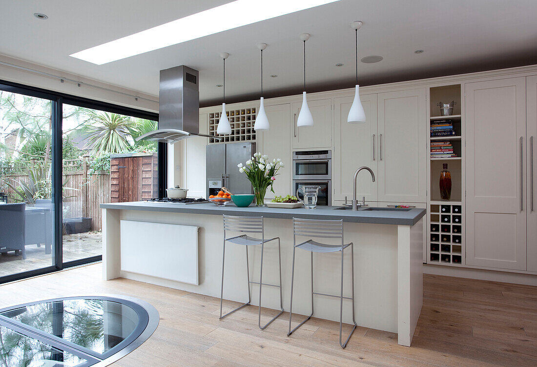 White fitted kitchen extension with pendant lights hanging above breakfast bar in London home, UK