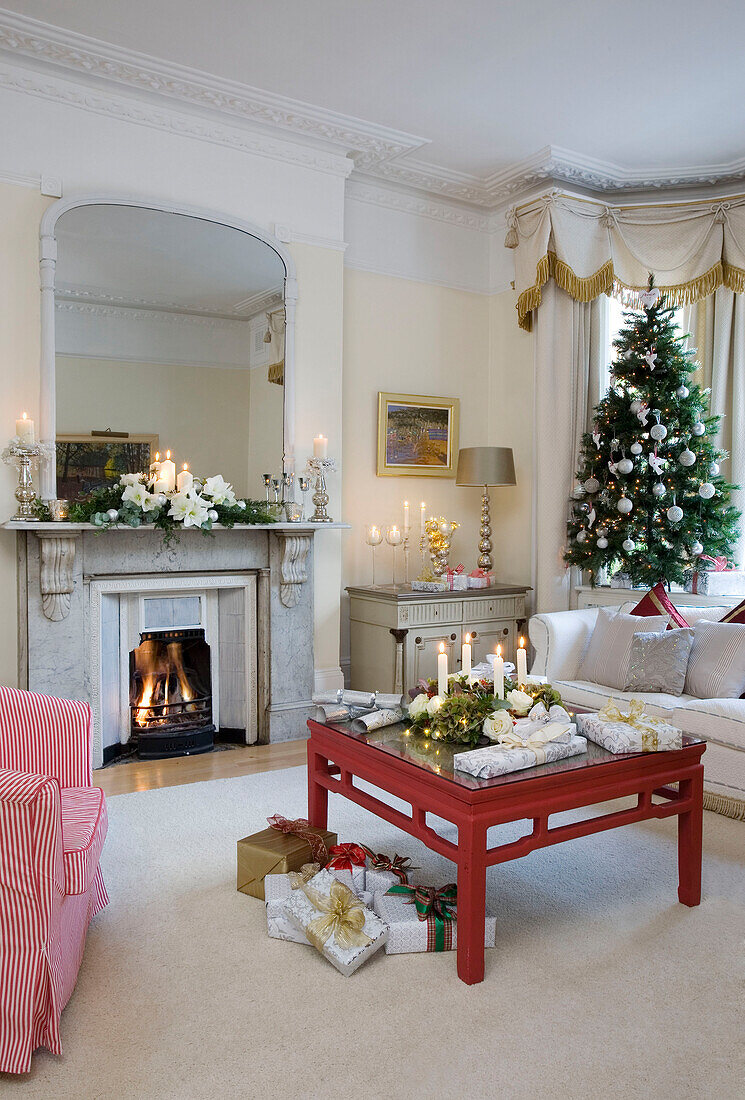 Lit candles and Christmas tree and presents on living room of London home, UK