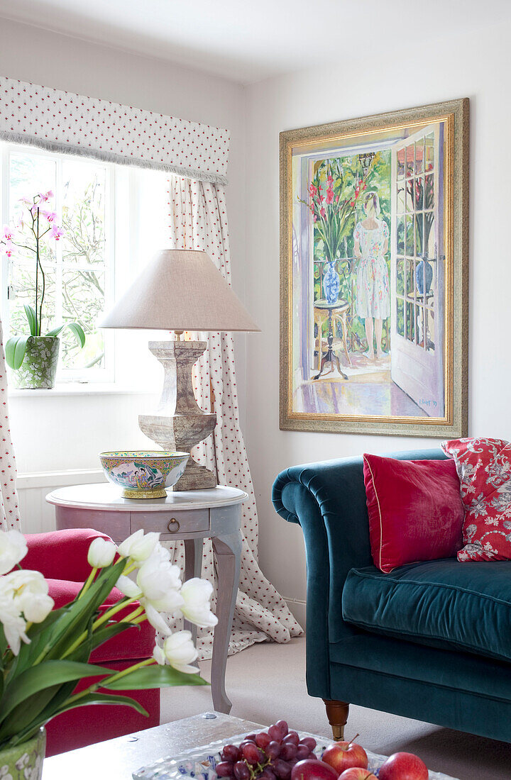 Lamp on side table with teal sofa at window in Sussex farmhouse, UK