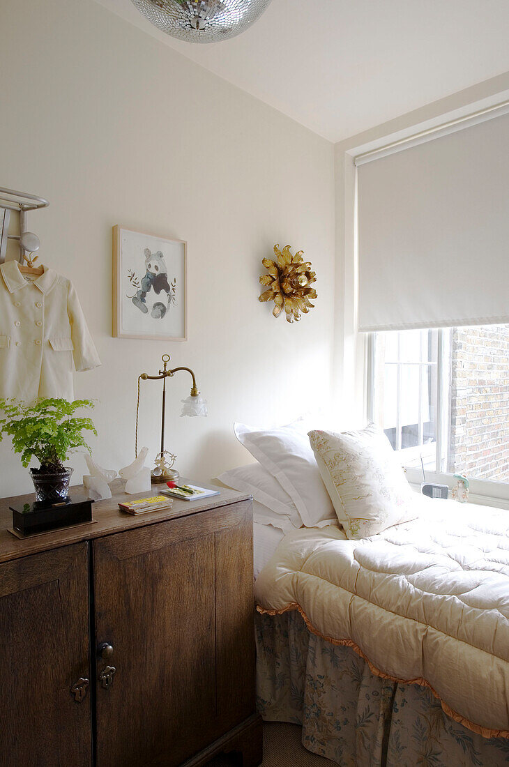 Single bed with duvet and wooden bedside cabinet at window of London home UK