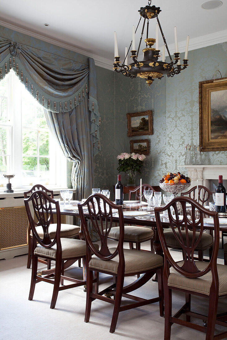 Chandelier above polished wood dining chairs at table in contemporary London townhouse, UK