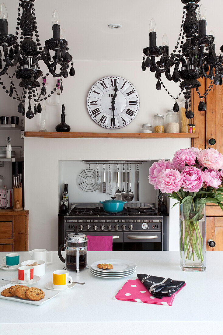 Matching chandeliers above breakfast bar in contemporary kitchen with clock above range oven in London home, UK