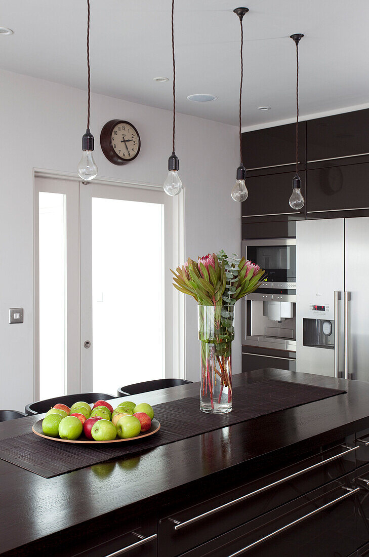 Bare lightbulbs above dark wood kitchen counter with apples and cut flowers in contemporary home, Hove, East Sussex, England, UK