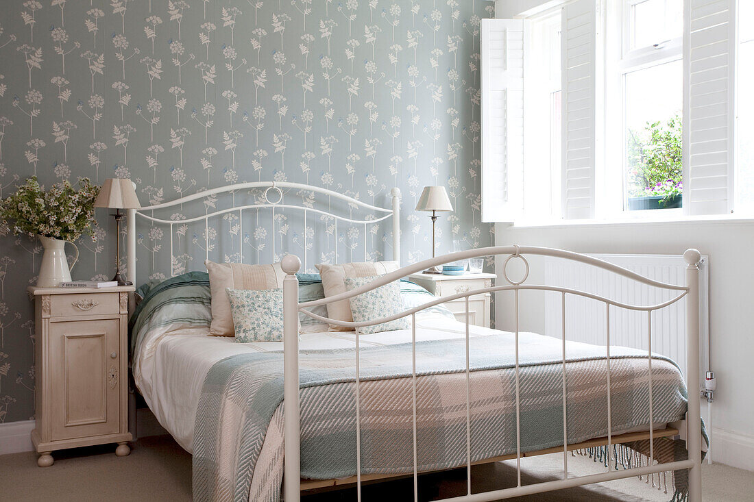 Hellblaue Schottenkaro-Decke auf einem weißen Metallbett mit Blumentapete in einem Haus in Surrey, England, Vereinigtes Königreich