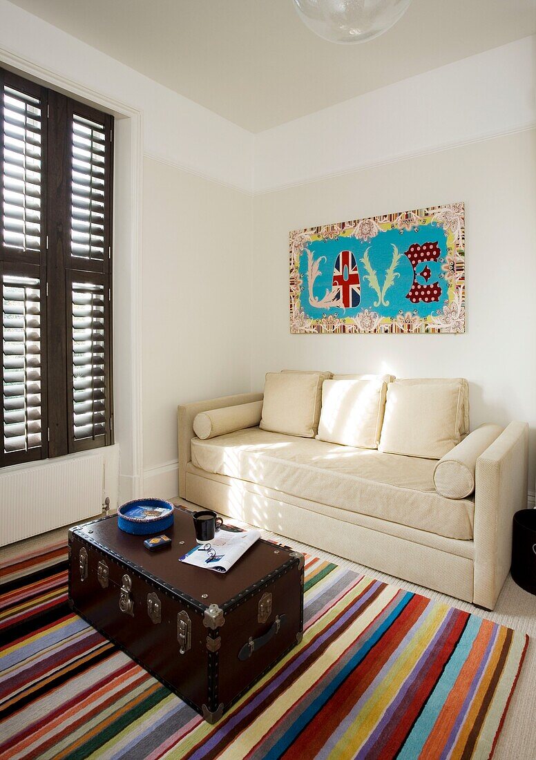 Sofa and artwork with travelling chest on striped rug in London home UK