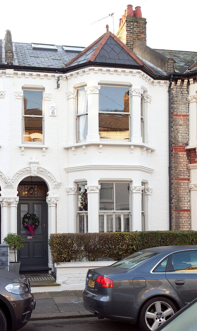 Cars parked in street outside white painted Victorian townhouse with Christa wreath on front door, London, UK