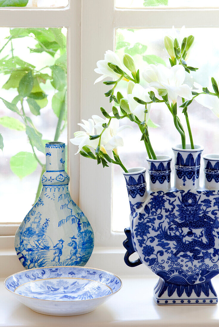 Einblütige Blumen in blauem und weißem Porzellan auf der Fensterbank eines Bauernhauses in Sussex, England, Vereinigtes Königreich