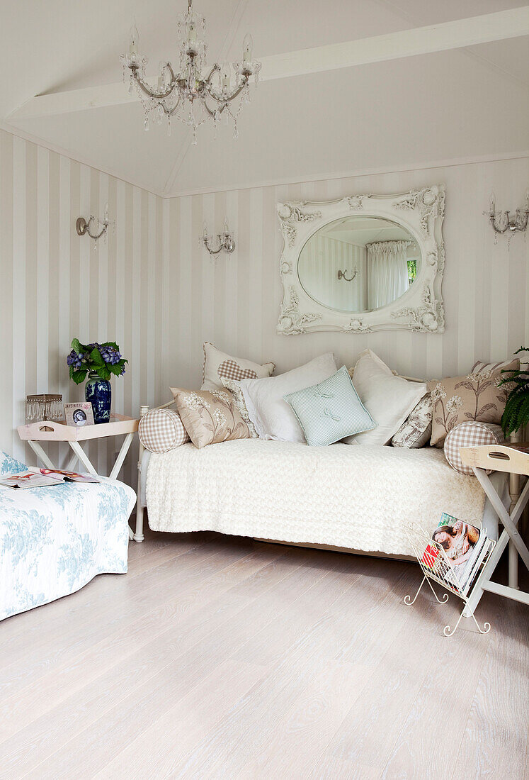 Ovaler Spiegel mit gestreifter Tapete im Wohnzimmer mit Kissen auf dem Sofa in einem Landhaus in Kent, England, UK