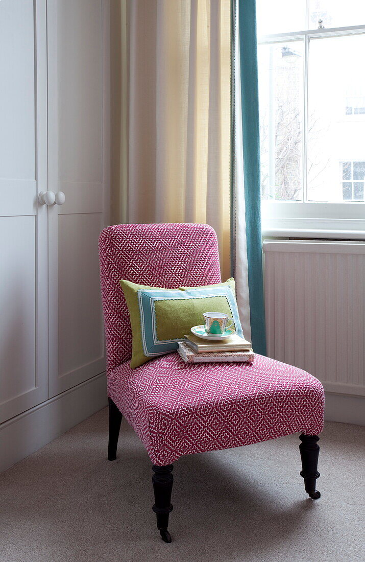 Teetasse und Bücher mit appliziertem Kissen auf einem gepolsterten Stuhl im Schlafzimmer in London, England, UK