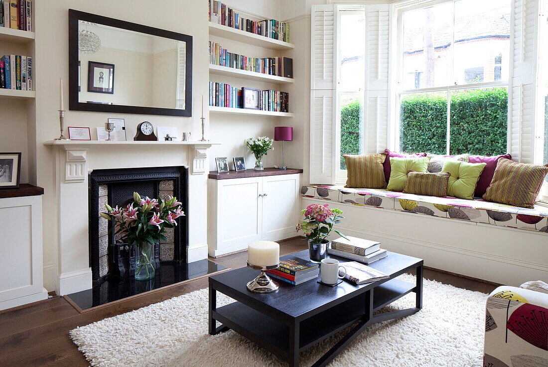 Eingelassene Bücherregale mit viktorianischem Kamin im Wohnzimmer mit gepolsterter Fensterbank in einem Stadthaus in London, England, UK