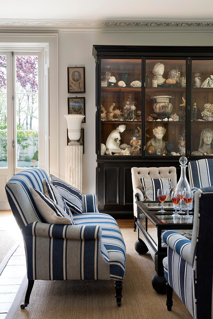 Blau-weißes Sofa und Vitrine mit historischen Artefakten im Salon eines Landhauses in Sussex, England UK