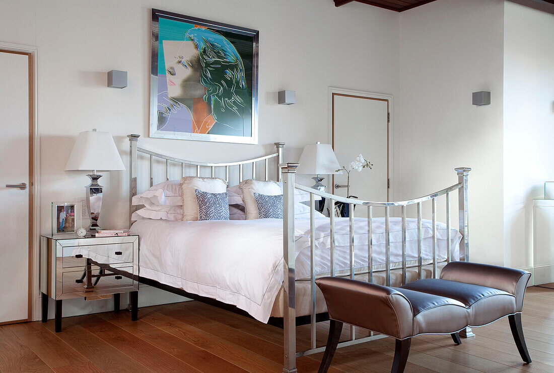 Chrome bed with modern art and footstool in Berkshire warehouse conversion, England, UK