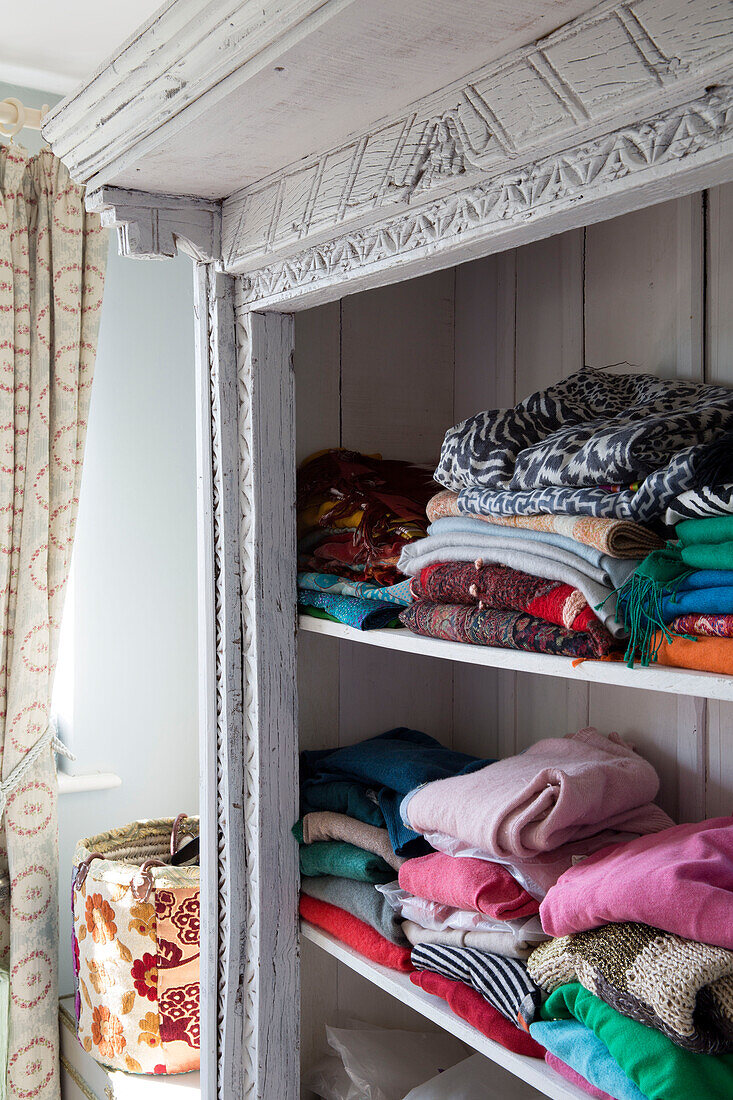 Folded jumpers on storage shelves in bedroom of Sussex home England UK