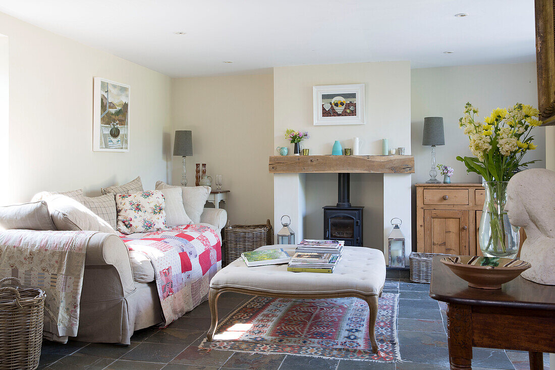 Cream ottoman and sofa with patchwork blanket in flagstone living room of Dorset cottage, England, UK