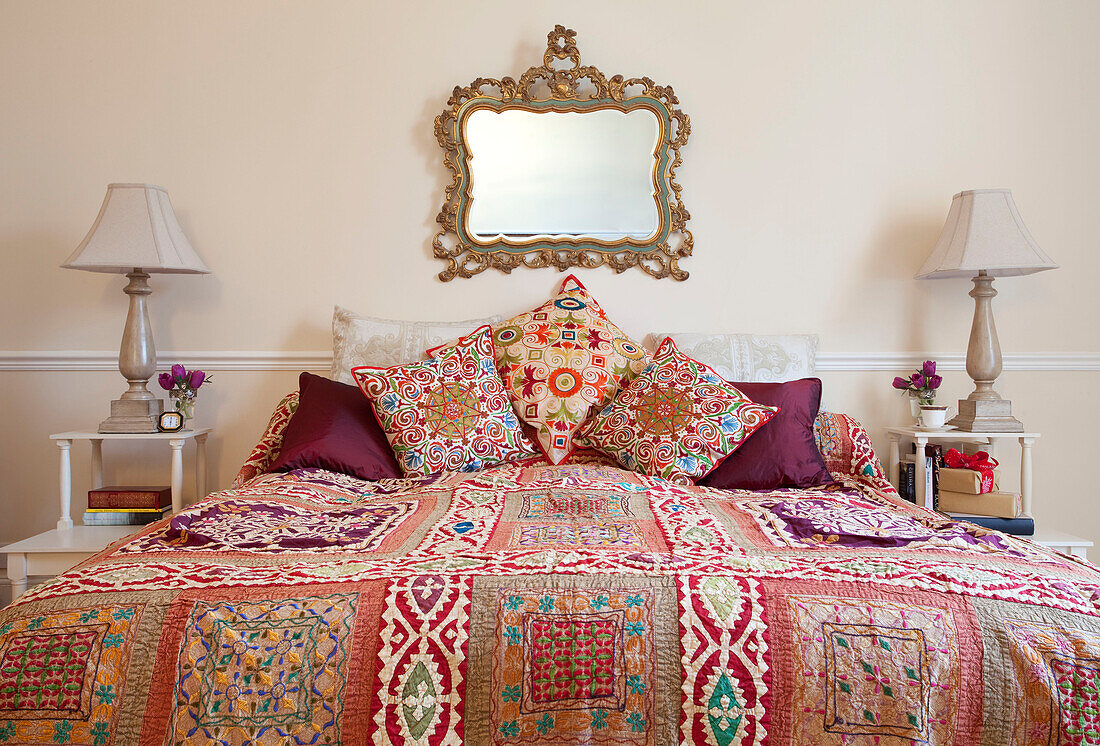 Ornate mirror above colourful quilted bed with matching lamps in West Sussex home, England, UK