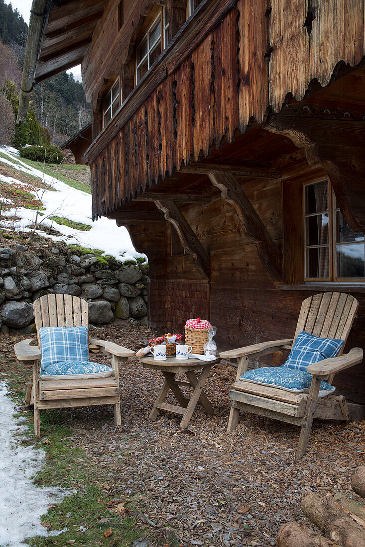 Stühle und Tisch unter dem geschnitzten Balkon eines Bergchalets, Chateau-d'Oex, Waadt, Schweiz