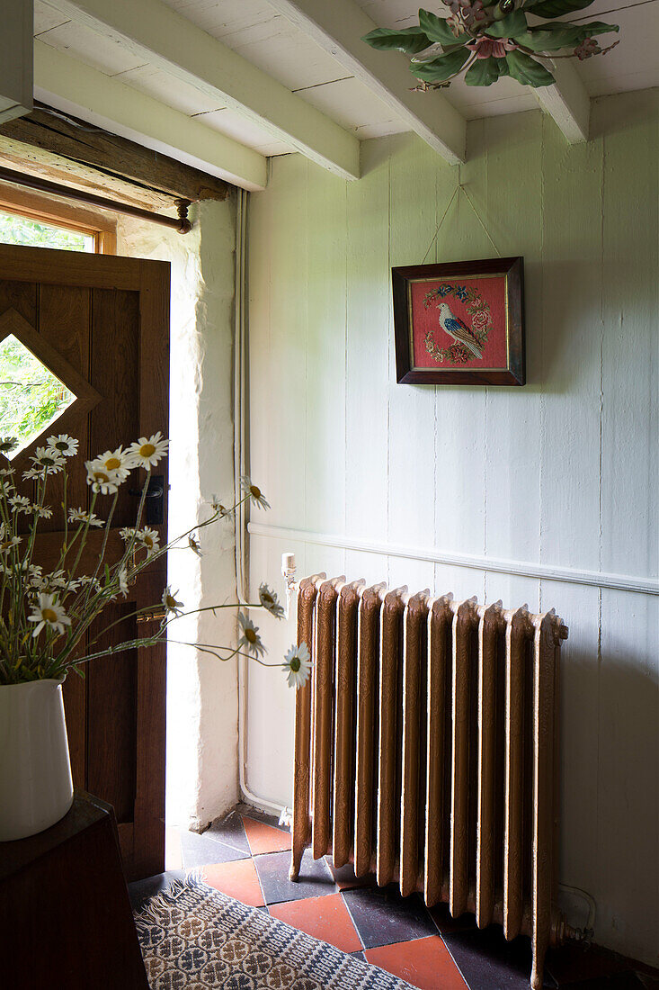 Cut daisies and radiator in tiled entrance hallway of Ceredigion cottage Wales UK
