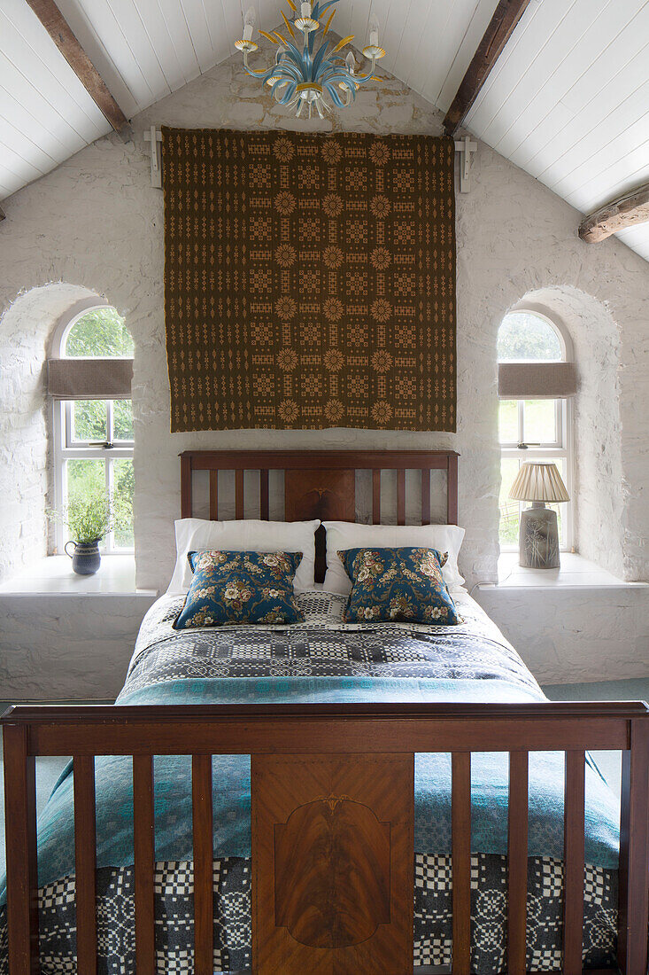 Arched windows with wooden double bed and wall hanging in Ceredigion cottage Wales UK