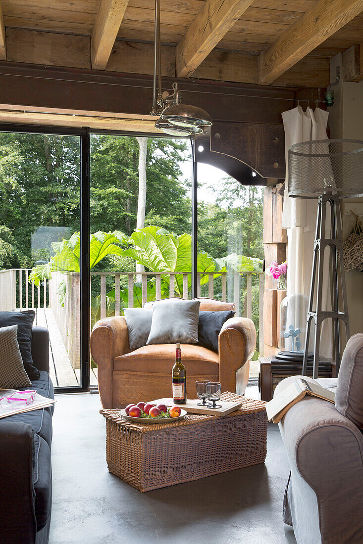 Weinflasche und Gläser auf einem Couchtisch aus Weidengeflecht mit Sessel am Fenster in einem französischen Bauernhaus-Wohnzimmer