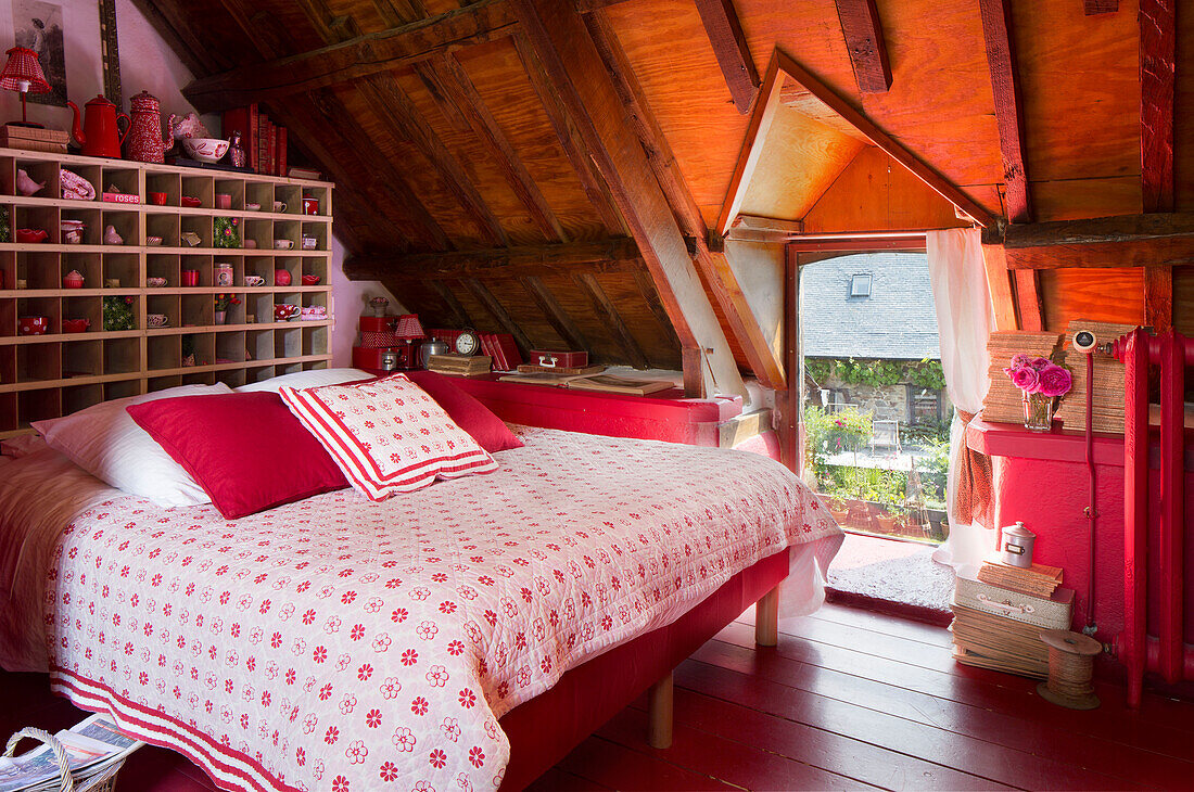 Floral quilt cover on double bed with storage shelves at dormer window in French farmhouse