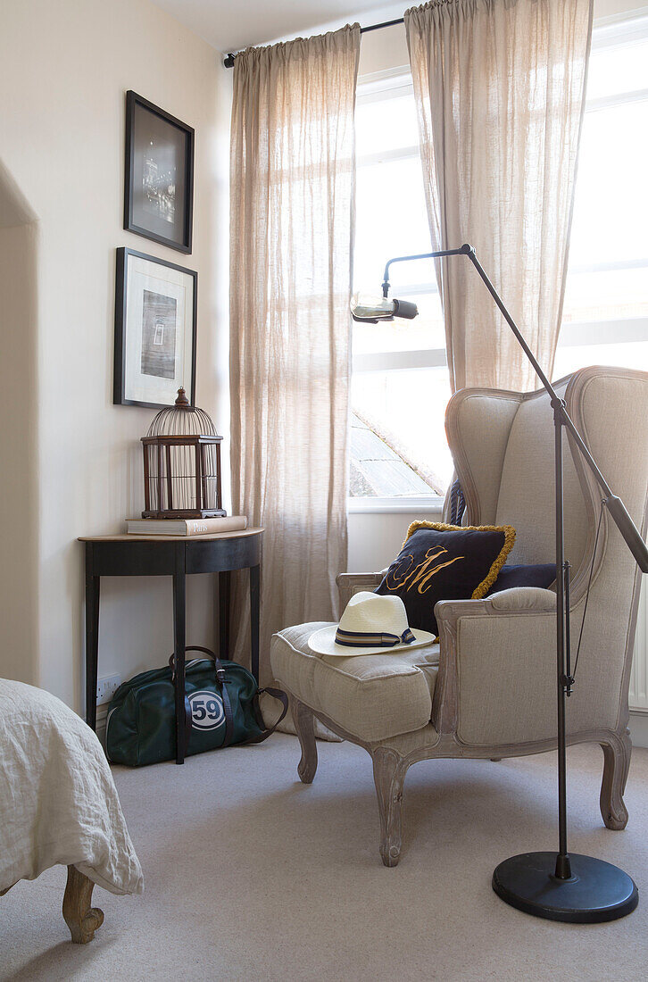 Cream armchair with sunhat and demi-lune table at window in Twickenham townhouse, Middlesex, England, UK