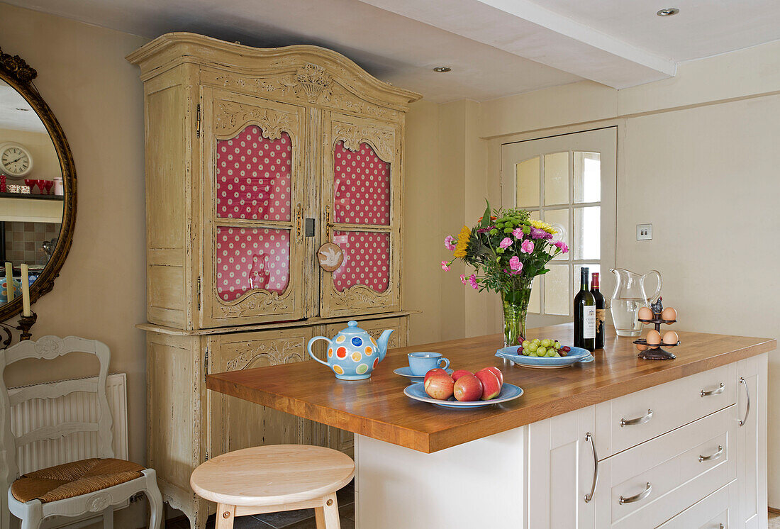 Spotted fabric in kitchen dresser with fruit and cut flowers on wooden workbench in UK home