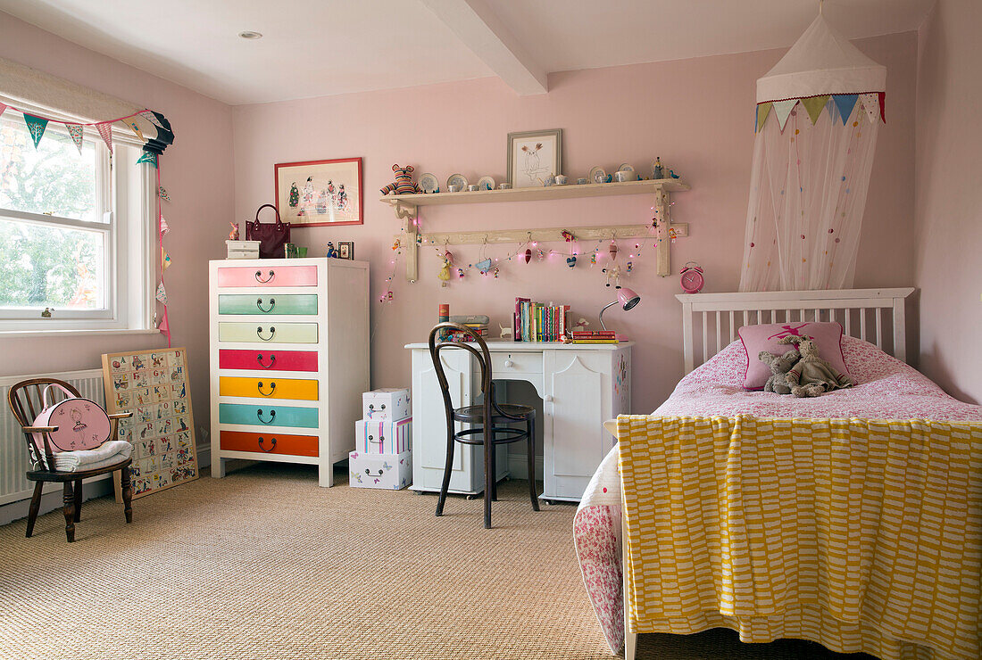 Single bed with desk and painted drawers in pastel pink girl's bedroom of London home,  England,  UK