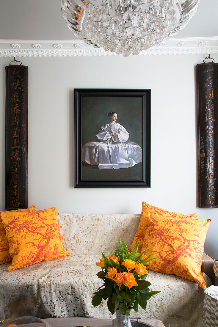 Chinesische Kalligraphie und Kunstwerke über einem Sofa mit gelb gemusterten Kissen in einem Haus in London, England, Vereinigtes Königreich