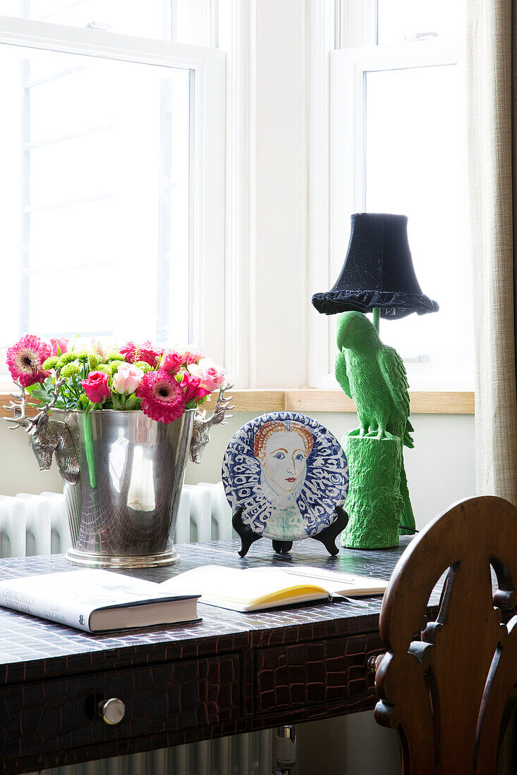 Schnittblumen in Eiskühler mit dekorativem Teller und Scherzartikel-Lampe auf dem Schreibtisch in einem Haus in London, England, UK