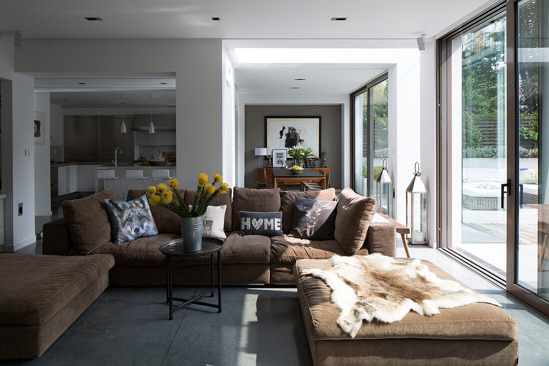 Sunlit open plan living room with brown sofa and animal skin rug in contemporary Sussex home, England, UK