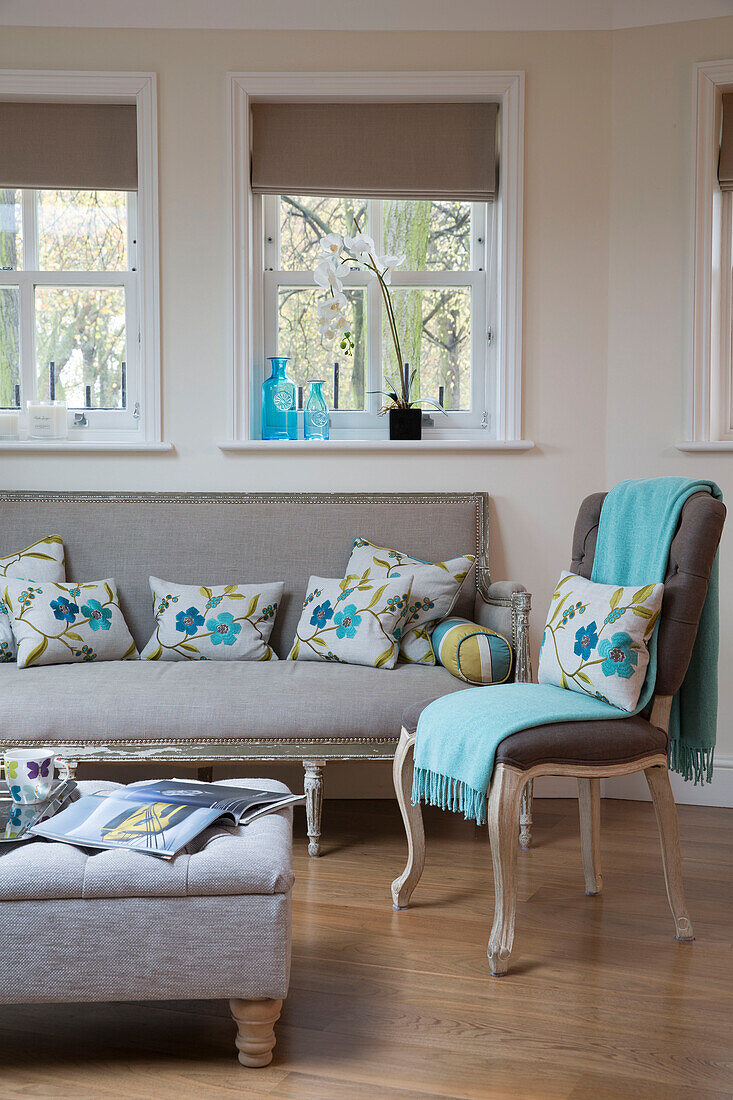 Floral cushions on sofa below windows in living room of London home   England   UK