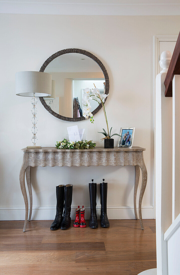 Orchidee und Lampe auf Konsole mit rundem Spiegel und Gummistiefeln im Flur eines Londoner Hauses England UK