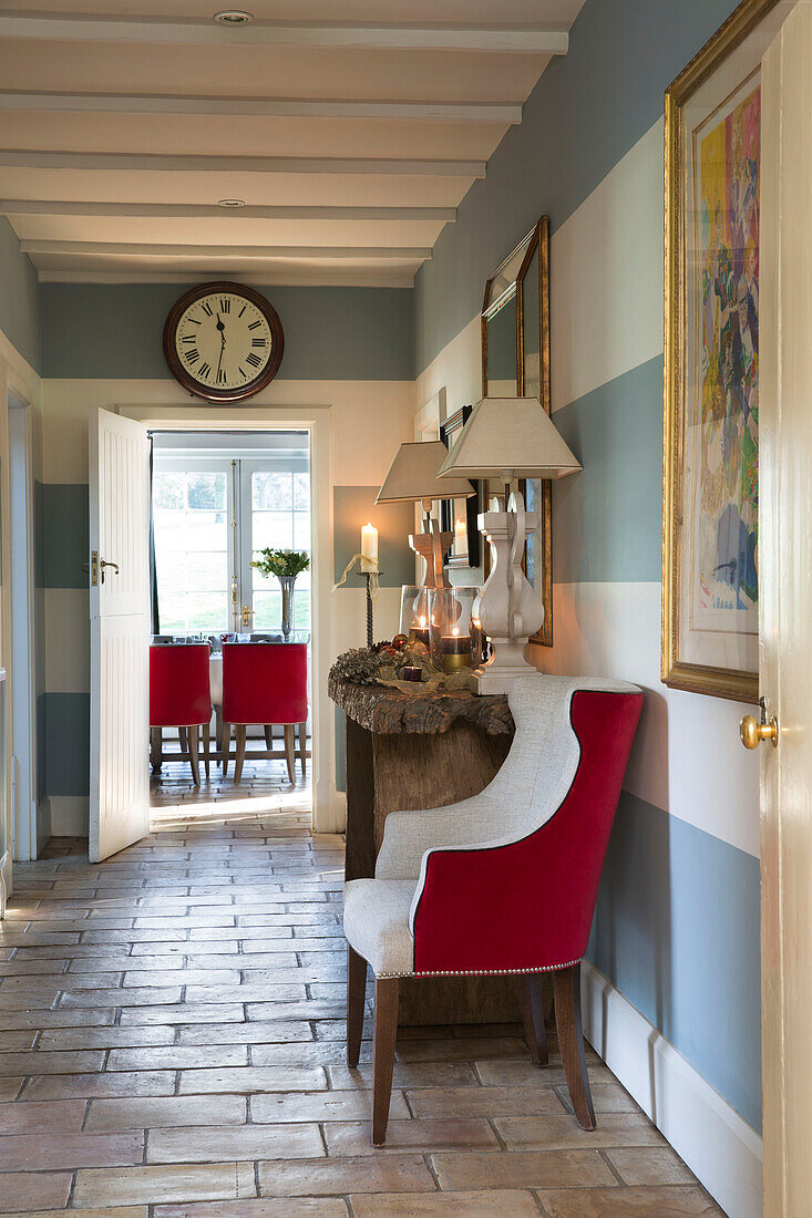 Red and white upholstered armchair with console in hallway with stone floor in Lymington home  Hampshire  UK