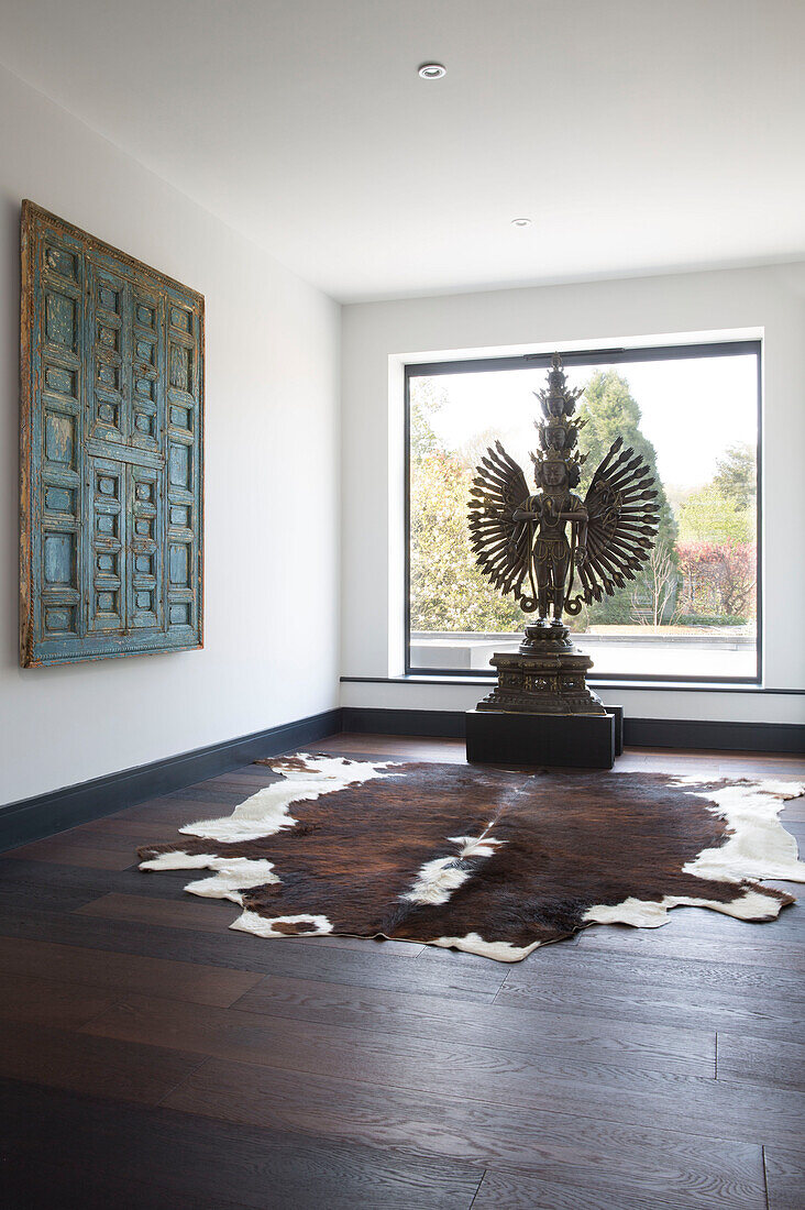 Hindu statue in front of picture window with ponyskin rug in London home,  England,  UK