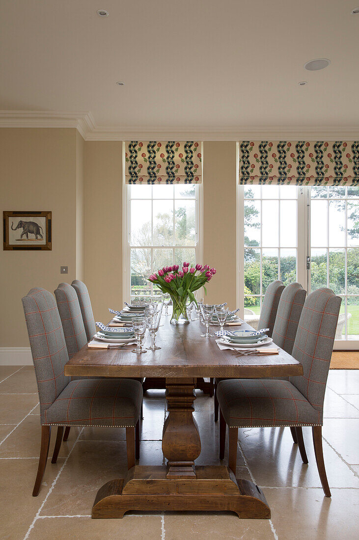 Upholstered chairs at wooden dining table with tulips in Pewsey country home Wiltshire England UK