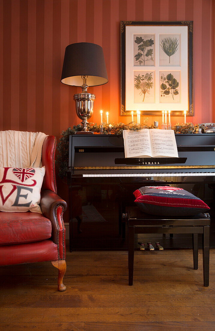 Roter Ledersessel neben dem Klavier mit brennenden Kerzen in einem Haus in Surrey England UK