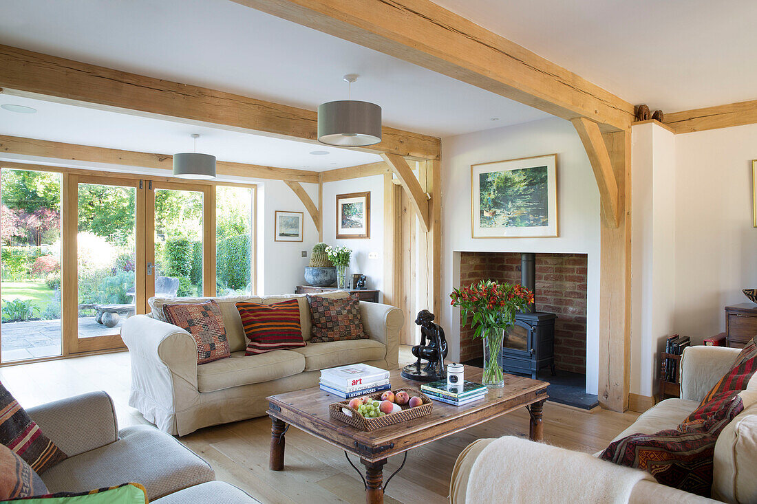 Lit woodburner and sofas with wooden coffee table in timber framed Surrey living room England UK