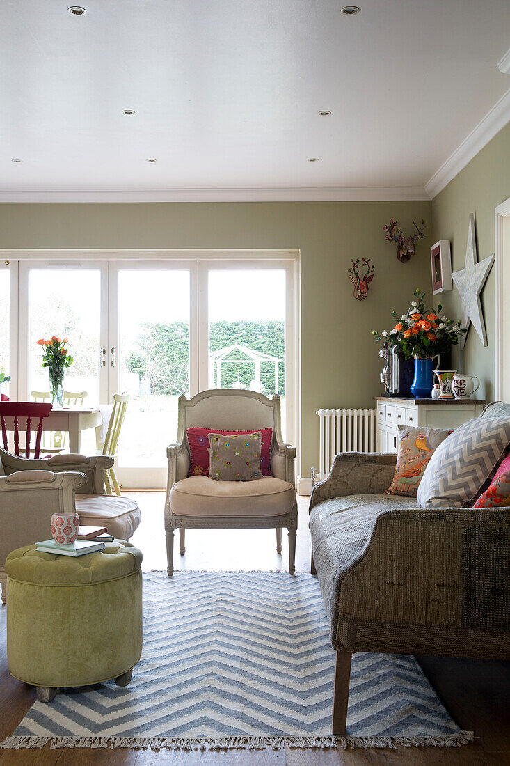 Sofa and armchair with buttoned footstool and patterned rug in living room of UK home