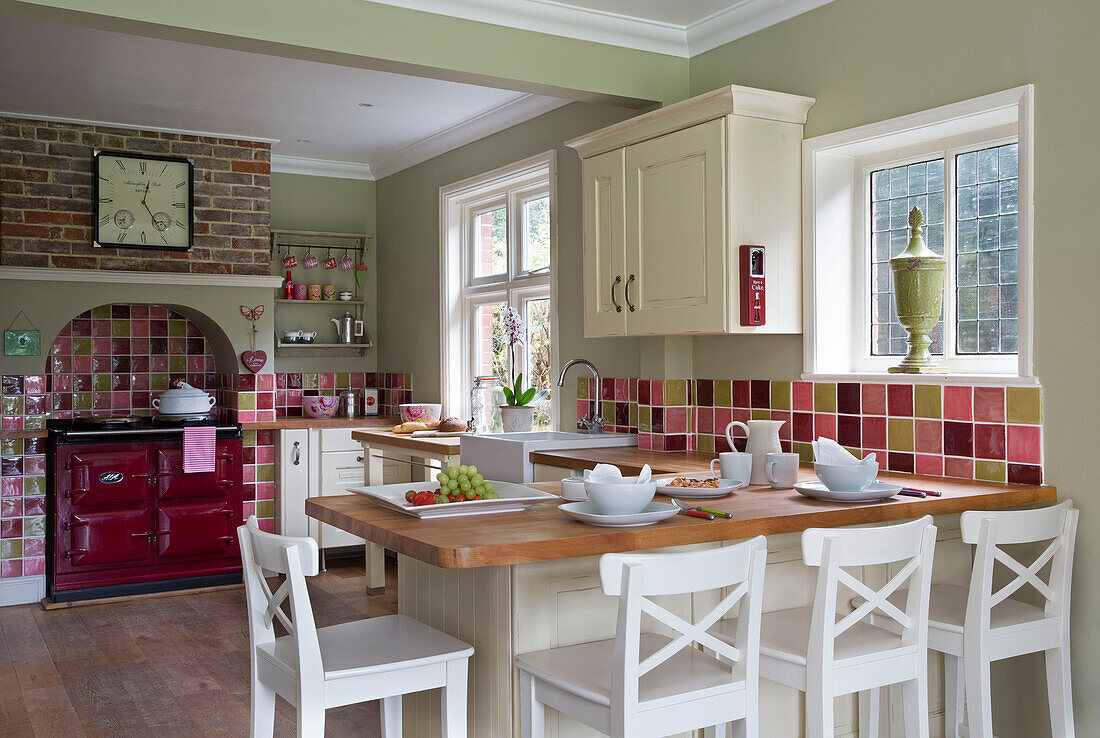 White barstools at wooden kitchen worktop in brightly tiled kitchen of UK home