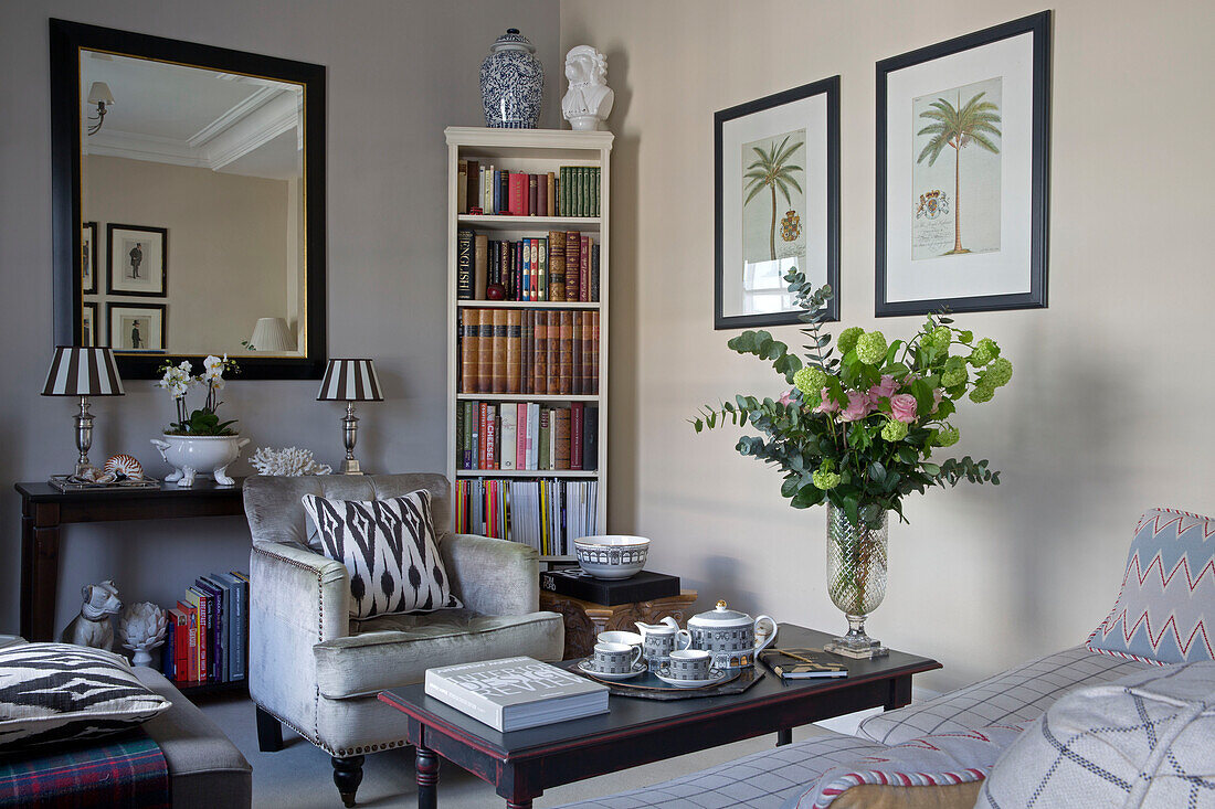 Grey armchair and bookcase with framed prints and cut flowers in London townhouse apartment UK