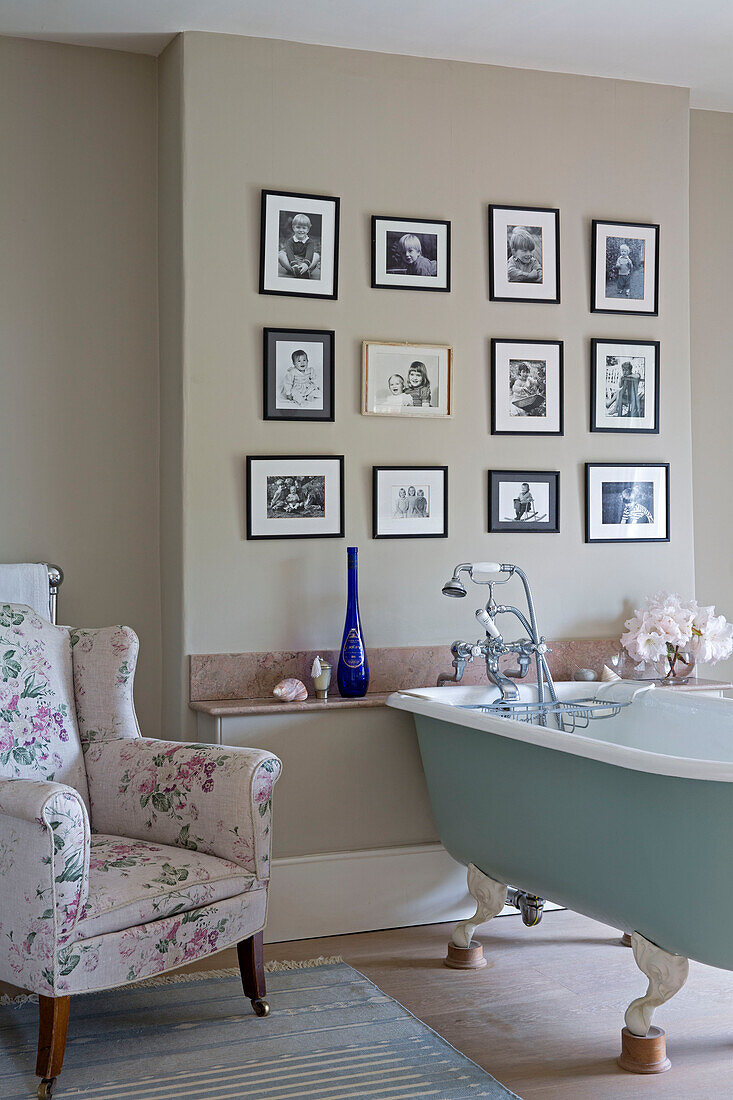 Light blue freestanding bath with floral armchair and family prints in Grade II listed Georgian country house in Shropshire England UK