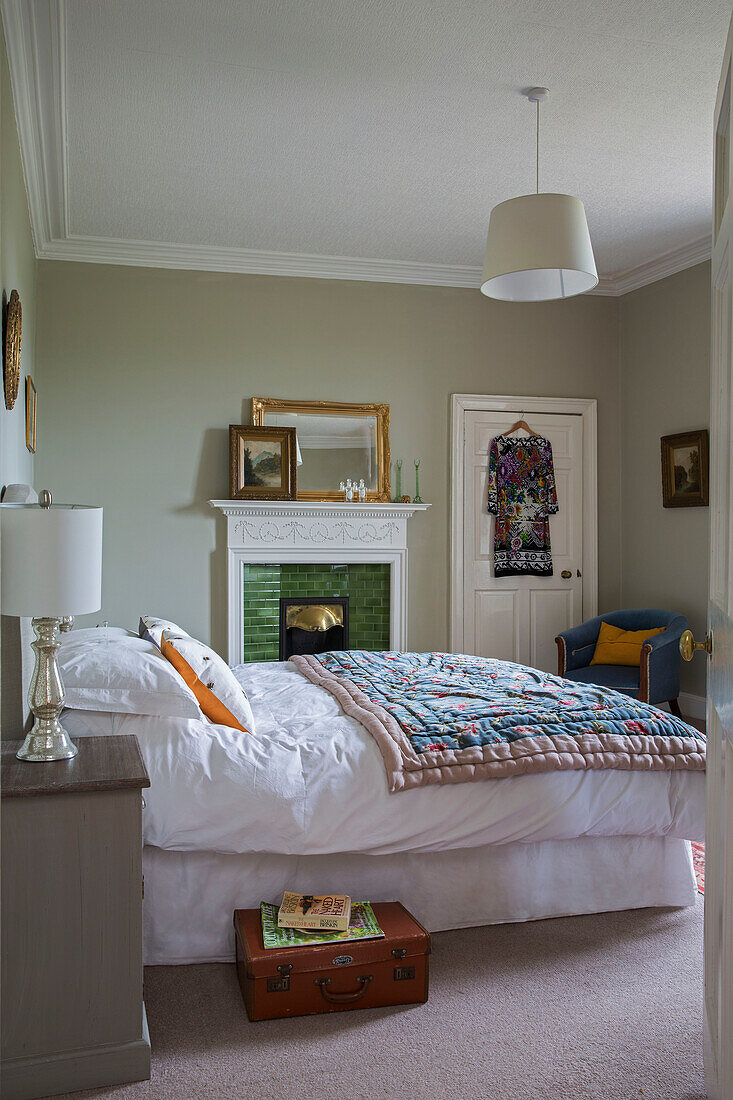 Dress hangs on back of door in double bedroom with quilted cover and vintage suitcase in Kelso home Scotland UK