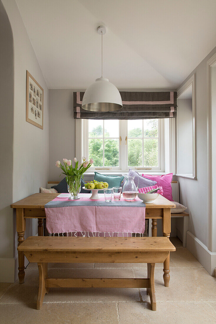 Rosa Tulpen auf Holztisch mit Bank in Fensternische eines Hauses in Gloucestershire, England UK