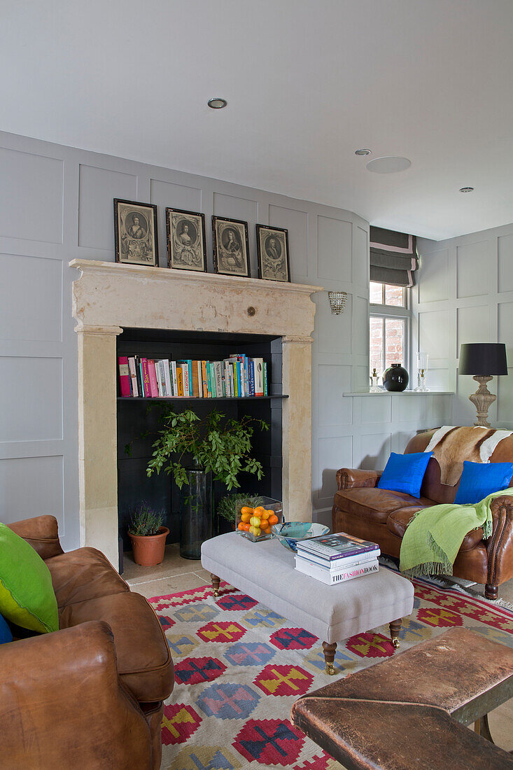 Fireplace repurposed as bookshelf with brown leather two-seater sofas in Gloucestershire living room England UK