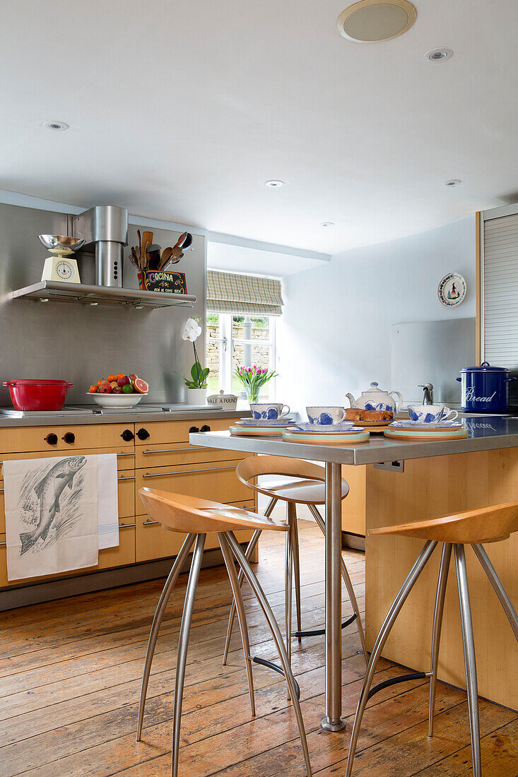 Wooden barstools at stainless steel breakfast bar in Gloucestershire farmhouse kitchen England UK