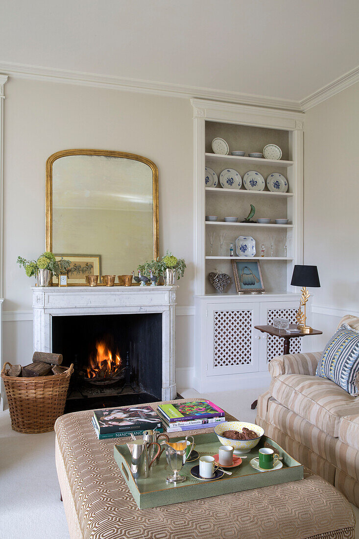 Gilt framed mirror above lit fire with tray on ottoman in Georgian rectory Northamptonshire England UK